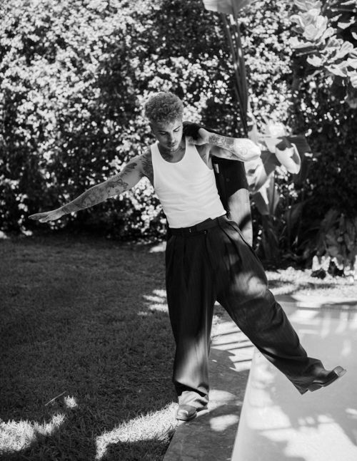 Black and white portrait of a man in a white tank top and dark trousers balancing by a swimming pool edge, photographed by Rose Marie Cromwell.