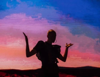 Silhouette of a person with outstretched arms standing against a textured pink and blue backdrop by Rose Marie Cromwell.