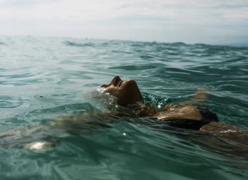 Person floating on their back in the ocean with water gently washing over their face and outstretched arms.