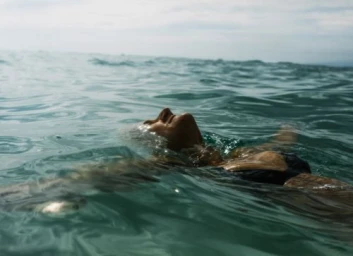 Person floating on their back in the ocean with water gently washing over their face and outstretched arms.