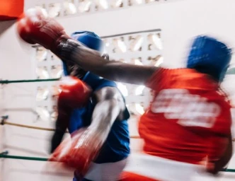 Two boxers sparring in a ring with heavy motion blur, one wearing red and the other blue.