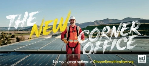 Adult male worker in safety gear stands on solar panels with mountain backdrop and ad campaign text for job opportunity advertisement.