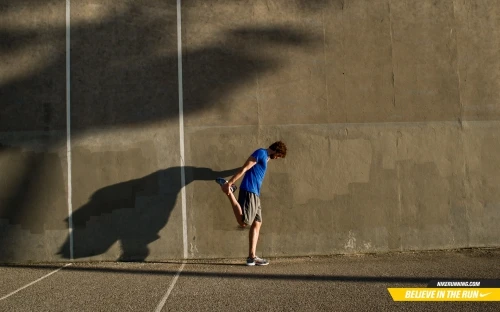 Man stretching against a weathered concrete wall, casting a large shadow on the surface.