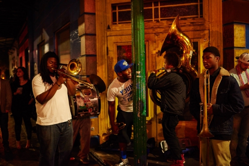 Nighttime street scene of a group of African-American musicians playing brass instruments, with passersby in the background.
