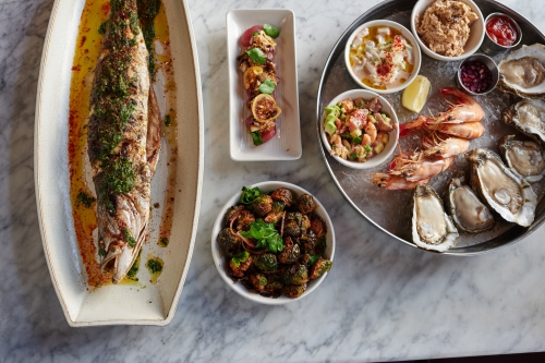 Overhead shot of a fresh seafood platter featuring grilled fish, oysters, shrimp, and various seafood salads served on a marble surface.