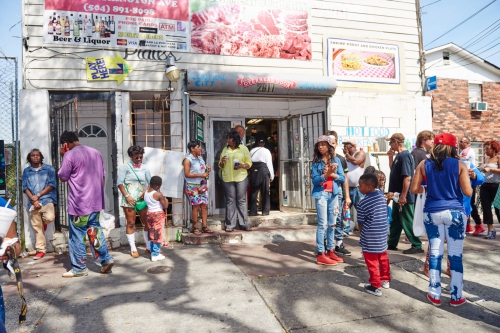 Outdoor gathering outside of Louisiana market with group of people. The building has storefront signage for food and beverages.