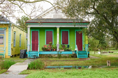 Colorful houses stand in New Orleans, Louisiana with a pond in the front yard and a wooden footbridge crossing the pond.