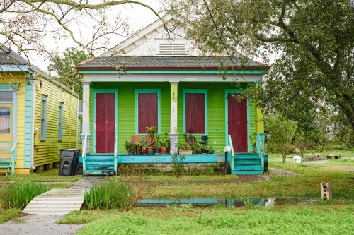 Colorful houses stand in New Orleans, Louisiana with a pond in the front yard and a wooden footbridge crossing the pond.
