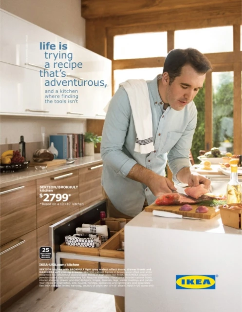 Man preparing food in a modern kitchen featuring wood cabinets, white countertops, and natural light from a large window.
