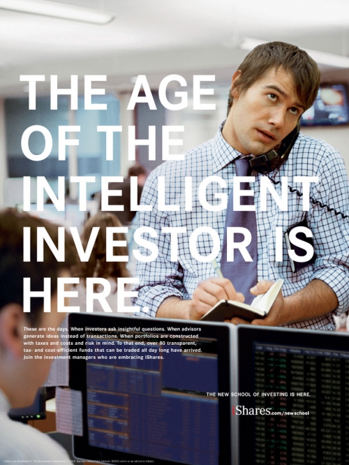 Man in shirt and tie talks on phone while writing in notebook in an office with computer screens showing financial data.
