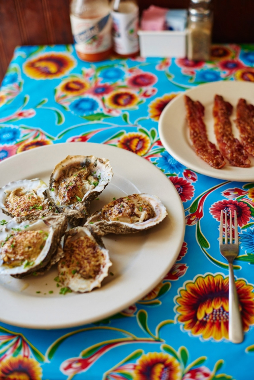 Overhead shot of oysters on a plate with bacon, set on a vibrant floral tablecloth. Ready to eat in an inviting setting.