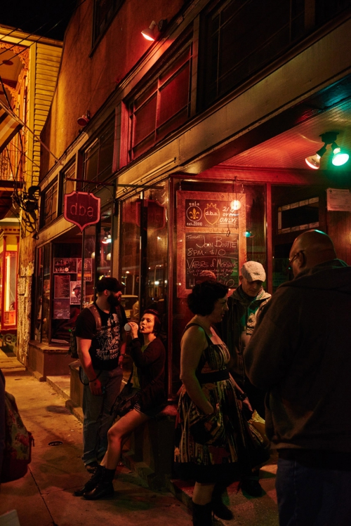 Night scene of a group of people outside a bar with red and green lights, creating a vibrant and lively atmosphere on the street.