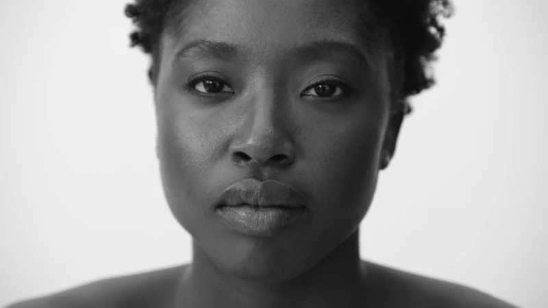 Close-up monochrome portrait of a Black woman looking directly at the camera against a plain white background.