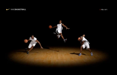 Three African American basketball players in action poses on a hardwood floor with a spotlight, set against a dark background. Nike branding visible.
