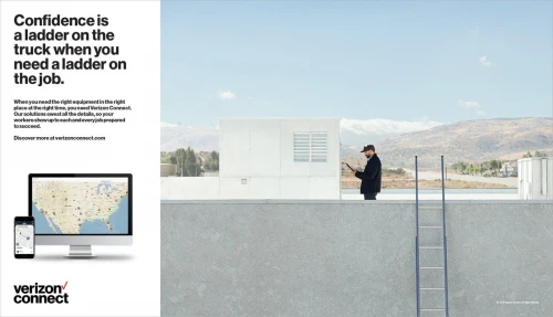Commercial shot of a man in a jacket and cap standing on a rooftop with a ladder, using a tablet, with mountains in the distance.