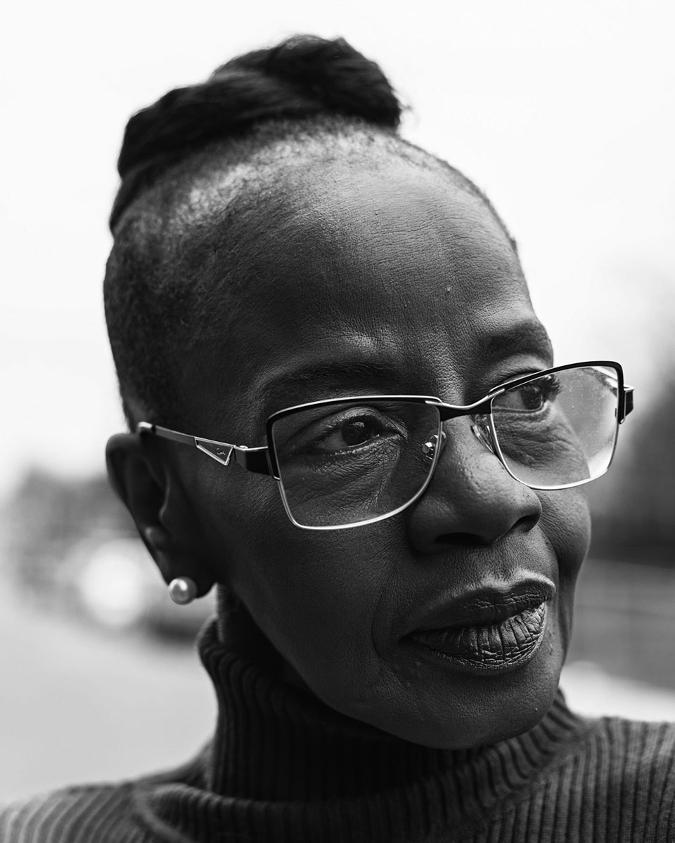 Black and white portrait of a stylish older Black woman wearing glasses and a turtleneck sweater, looking off to the side.