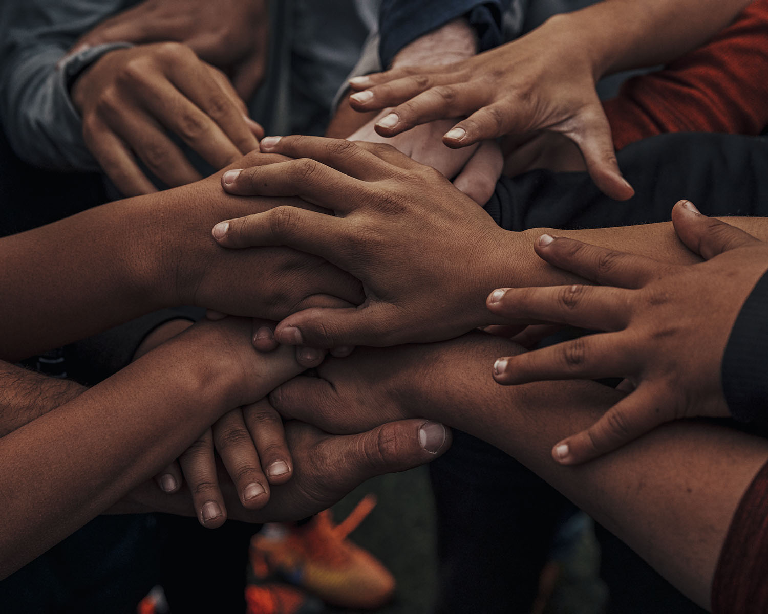 Multiple hands are piled on top of each other in a group of various skin tones and ages in a display of unity and togetherness.