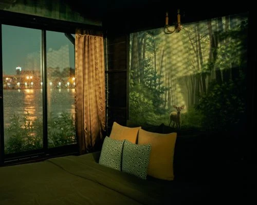 Bedroom interior featuring a bed with pillows, a nature mural of a forest with a deer, and a window view of a lake at dusk.