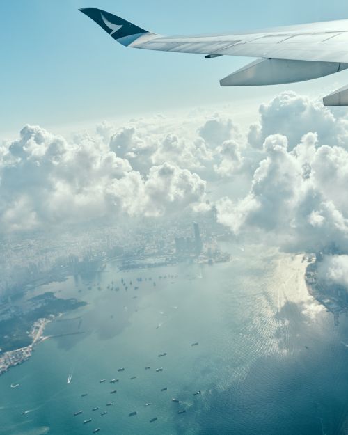 Aerial view from airplane window of wing above clouds, water, and city. Commercial aviation and travel concept.