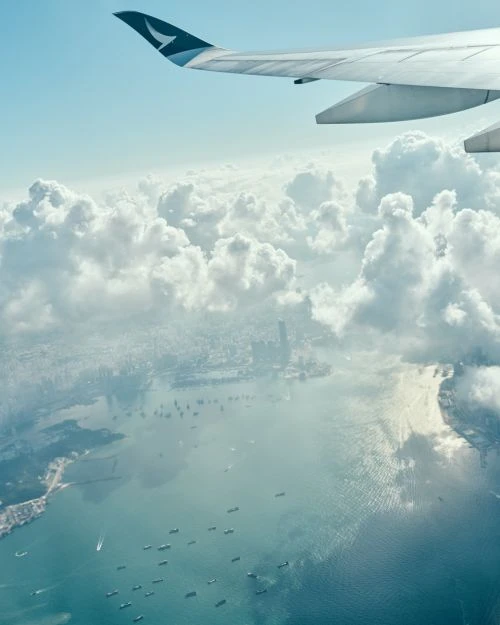 Aerial view from airplane window of wing above clouds, water, and city. Commercial aviation and travel concept.