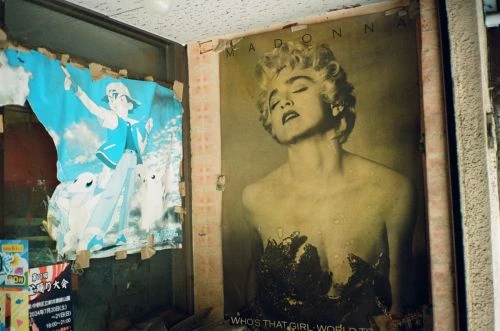 Posters adorn an interior corner: Madonna's vintage promo next to a weathered Pokémon graphic, creating a unique, contrasting pop culture display.
