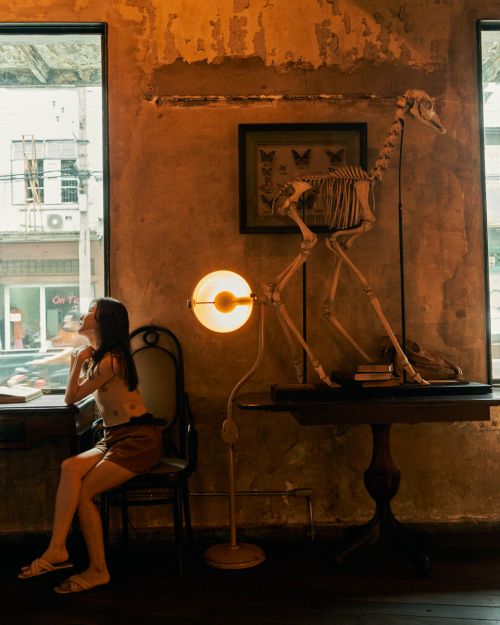 Woman sits by window in room with bone skeleton, lamp, and butterfly art, showcasing a blend of modern and artistic design elements.