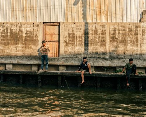 Three young men near a concrete canal wall with corrugated metal above, photographed by Balazs Gardi in Los Angeles.