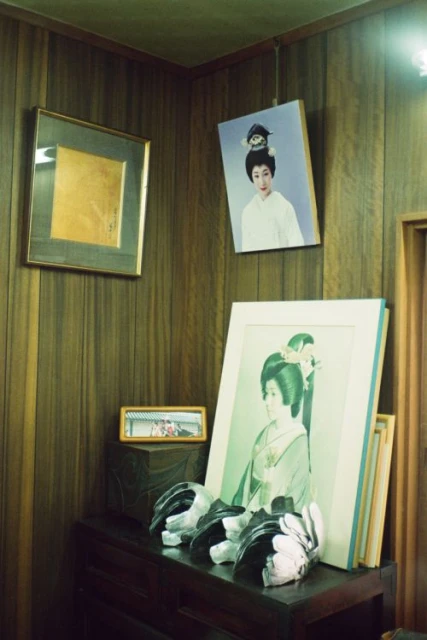 Indoor still life featuring framed portraits on a wooden wall, with carved masks atop a dark wooden cabinet. Interior decor is classic.