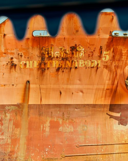 Close-up of a rusty, orange vessel with faded text and blue details, creating an abstract maritime view with weathered textures.