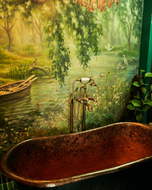 Luxurious bathroom featuring a copper bathtub and a pastoral mural showcasing a river scene with boat, birds, and lush greenery.