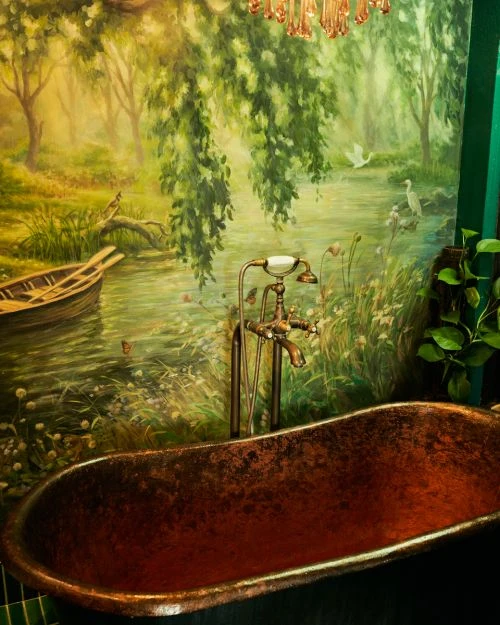 Luxurious bathroom featuring a copper bathtub and a pastoral mural showcasing a river scene with boat, birds, and lush greenery.