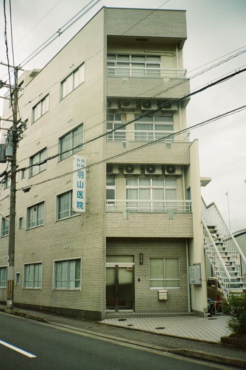Exterior view of a multi-story brick building with windows, air conditioning units, and stairs on the side in an urban environment.