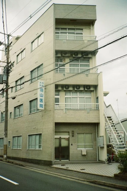 Exterior view of a multi-story brick building with windows, air conditioning units, and stairs on the side in an urban environment.