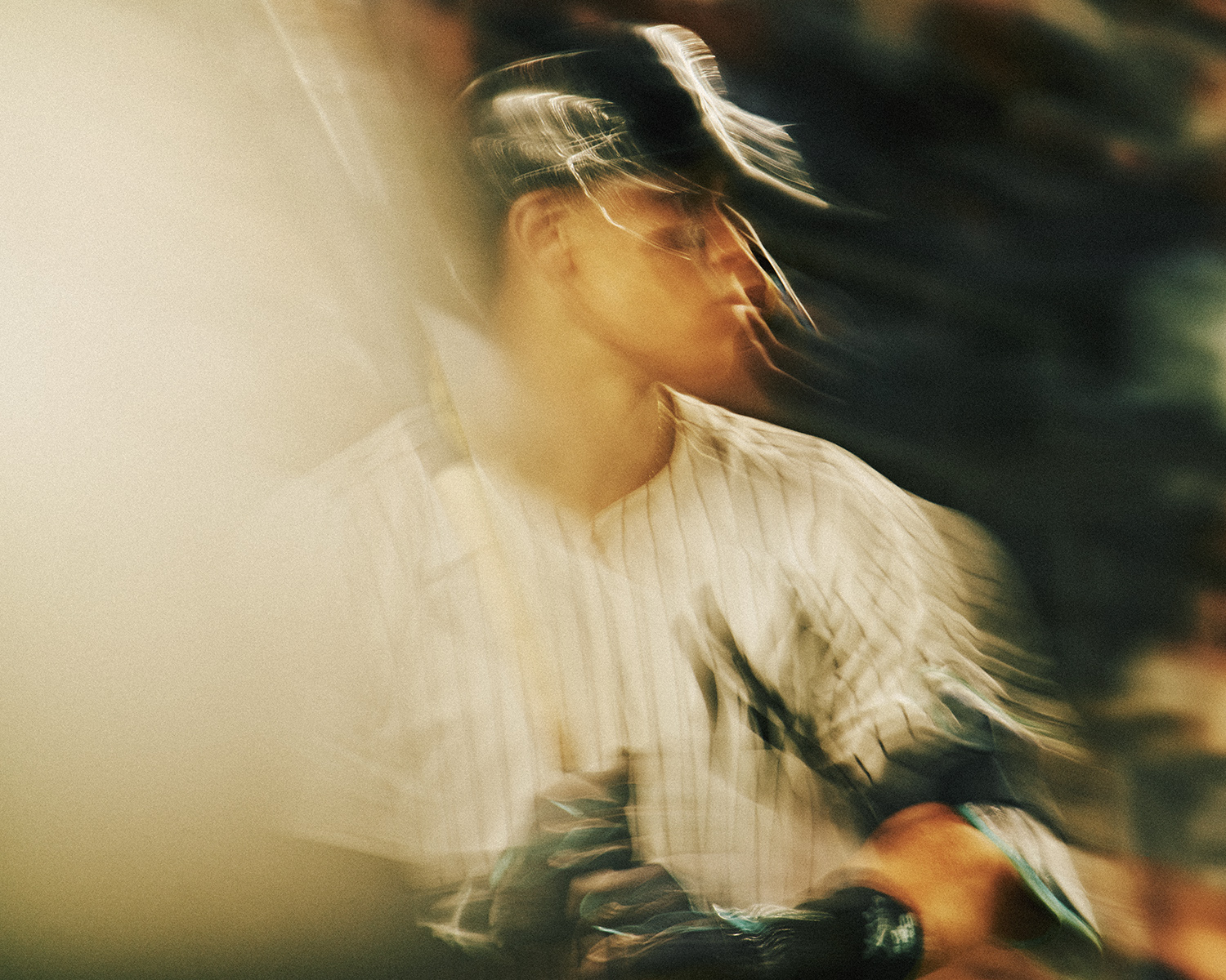 Male baseball player wearing a cap and striped uniform in blurred action on the field, swinging a bat with focused concentration.
