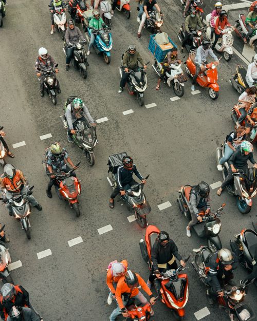 Aerial view showcases a bustling city street filled with numerous people riding scooters and motorbikes, creating a vibrant urban scene.