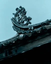 Detailed view of ornate traditional Asian roof tile architecture against a pale blue sky by Balazs Gardi.
