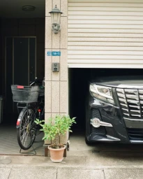 A black luxury car parked in a garage next to a bicycle with a front basket and a small potted plant in Los Angeles.