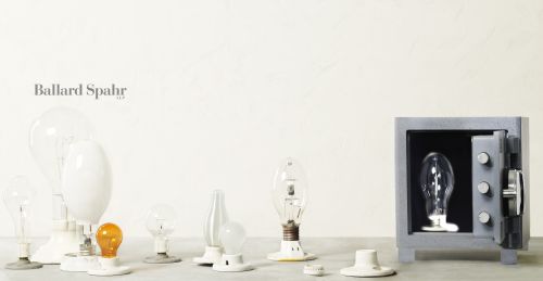 Still life of assorted lightbulbs, some in open safe, against a plain white wall, creating a clean, conceptual scene.