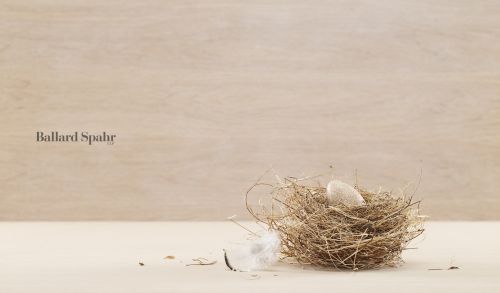 Close-up of a bird's nest with a single egg and a small white feather against a light beige background, creating a minimalist composition.