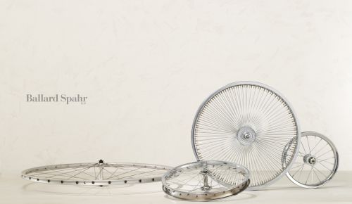 Four bicycle wheels with chrome rims and spokes arranged on a white surface against a textured white background.