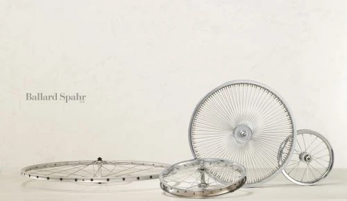 Four bicycle wheels with chrome rims and spokes arranged on a white surface against a textured white background.