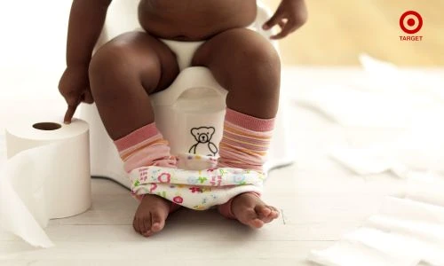 Child sitting on a potty with a roll of toilet paper nearby in a brightly lit indoor setting. Potty training and childcare imagery.