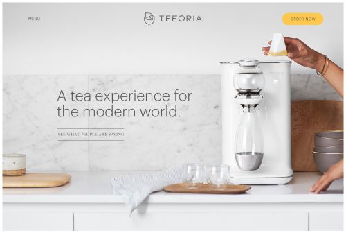 Woman preparing tea with a white tea maker on a bright counter with bowls and glasses in a modern kitchen setting, clean aesthetic.
