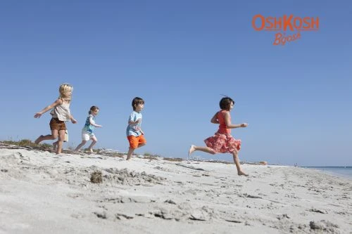 Four children running across a sandy beach under a clear blue sky, photographed by Laurie Frankel.