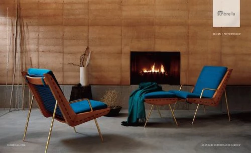 Interior featuring two mid-century modern lounge chairs with blue cushions, brass legs, and a fireplace in the background. 