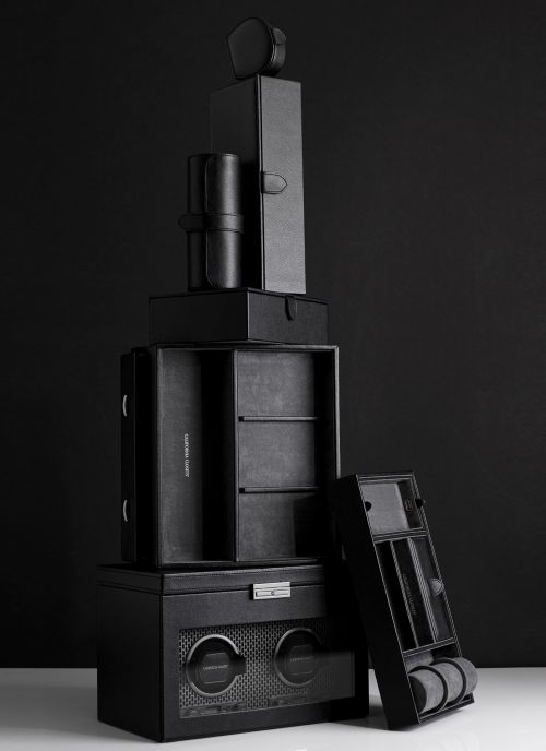 Stack of black leather watch and jewelry storage boxes against a dark background. Neutral product shot highlighting textures and craftsmanship.
