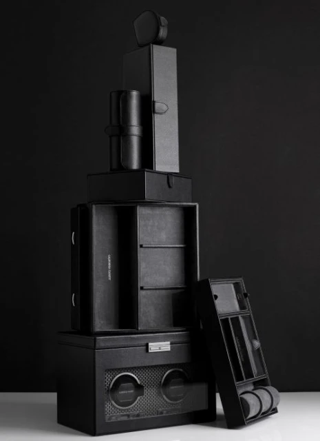 Stack of black leather watch and jewelry storage boxes against a dark background. Neutral product shot highlighting textures and craftsmanship.
