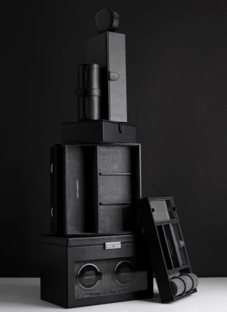 Stack of black leather watch and jewelry storage boxes against a dark background. Neutral product shot highlighting textures and craftsmanship.