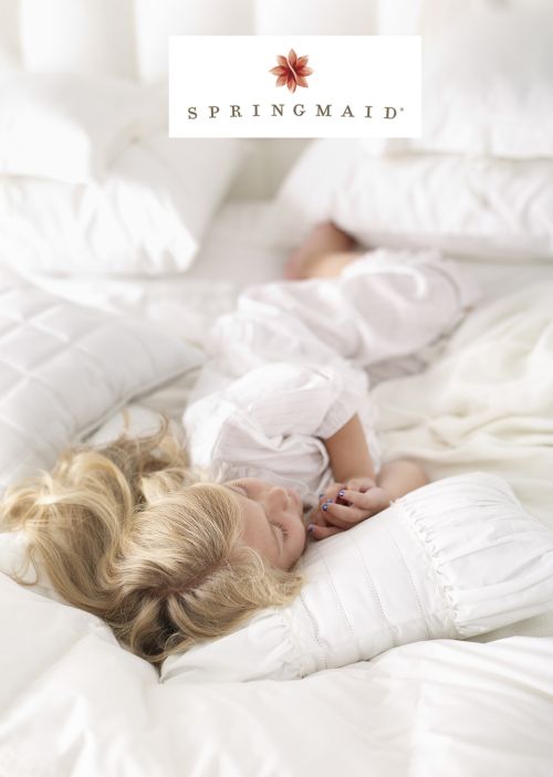 Blonde child in white dress sleeps on a white bed with white pillows, a white comforter, and a white headboard; Springmaid logo.