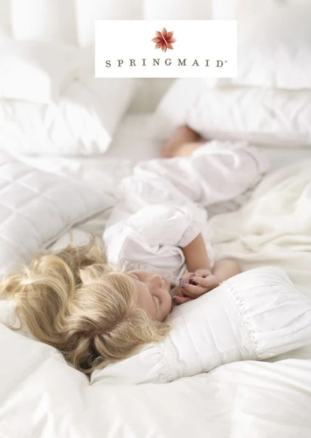 Blonde child in white dress sleeps on a white bed with white pillows, a white comforter, and a white headboard; Springmaid logo.